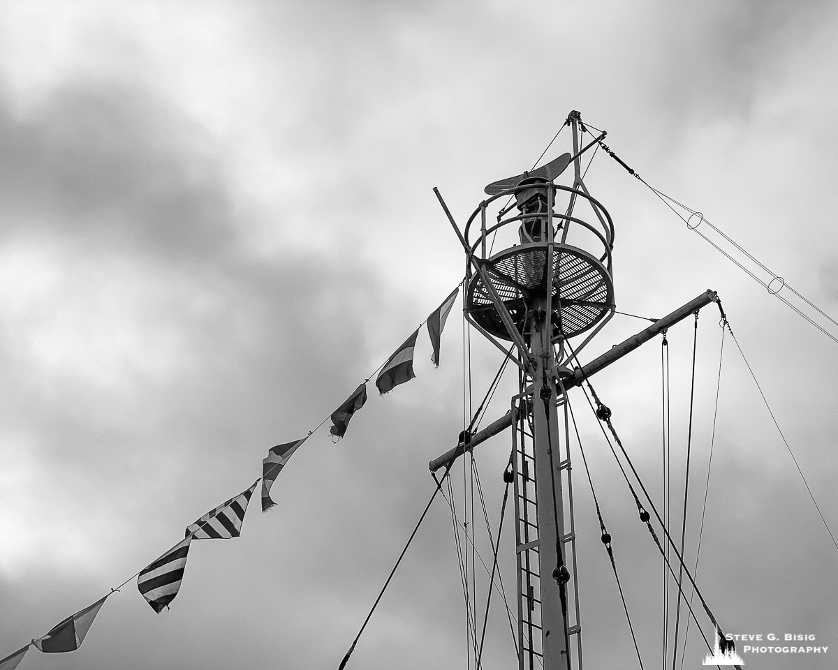 A black and white mobile photograph of the mast of the Lightship Columbia moored along the historic waterfront in Astoria, Oregon.
