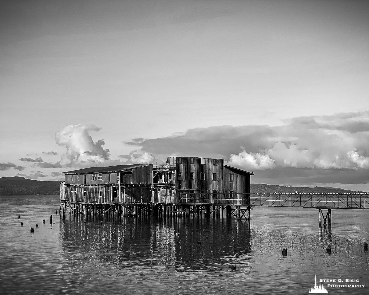 A black and white mobile photograph of an old wharf along the historic waterfront in Astoria, Oregon.