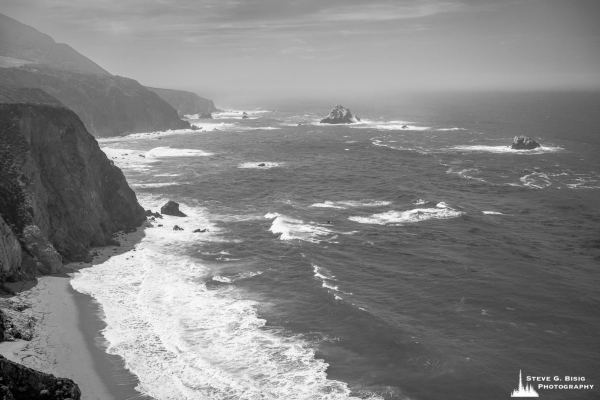A black and white landscape photograph of the Pacific Ocean and coastline along the Cabrillo Highway 1 near Bixby Creek, California.