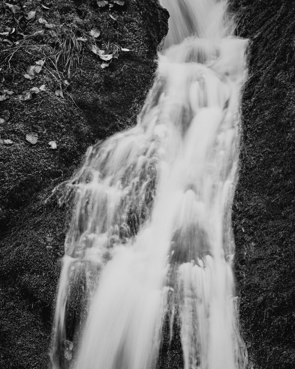 A narrow cascade shapes stone and softens light as it flows down the hillside. Every moment changes its form — water finding its way, translating persistence into grace.