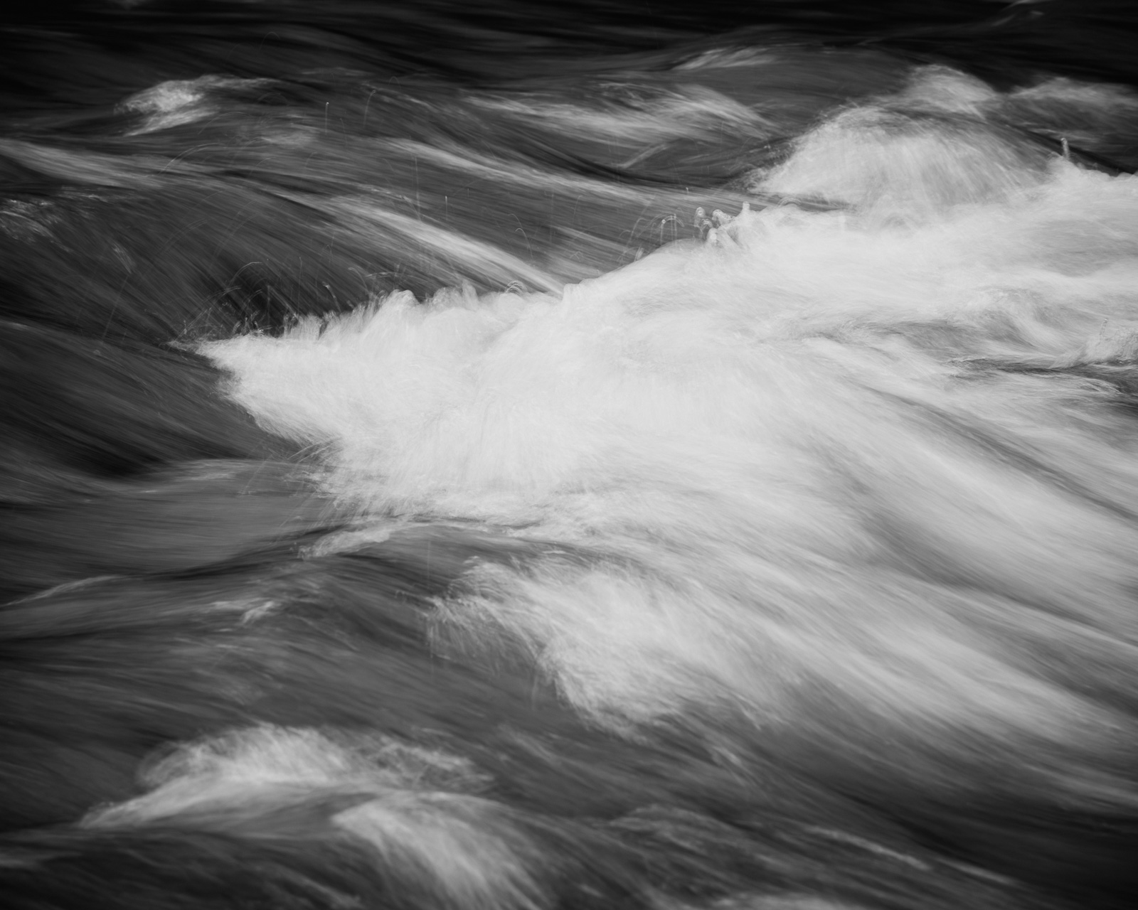 Bright water cuts diagonally through darker layers, where intersecting currents briefly gather before moving on.