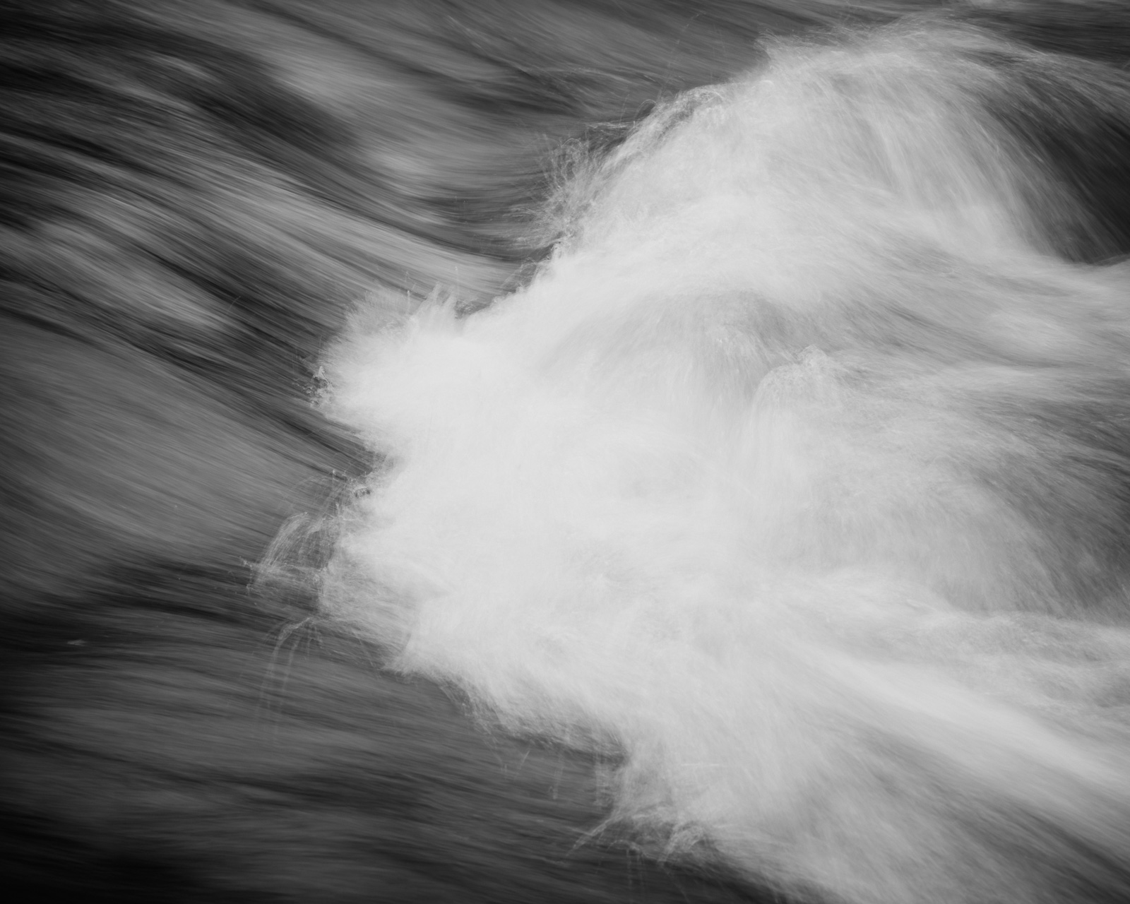 White water surges across the frame, its leading edge dissolving into darker currents as the flow presses onward.