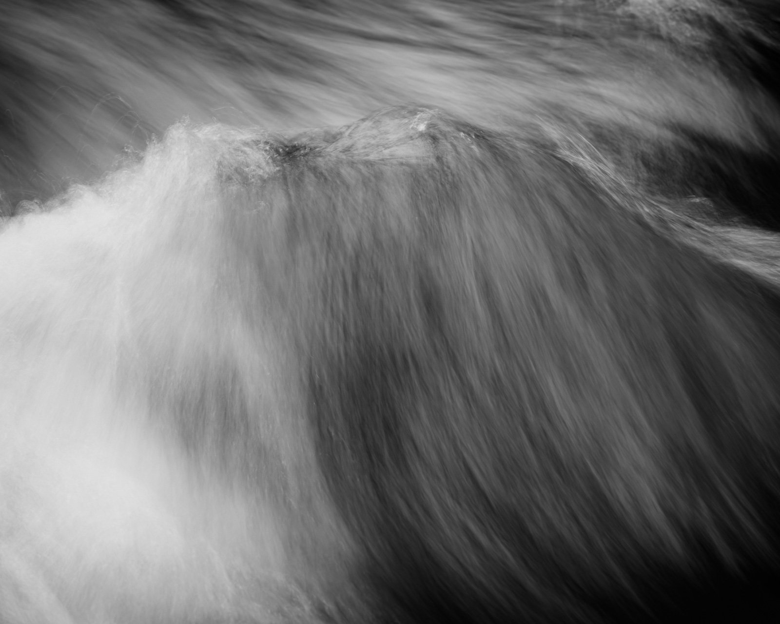 Water gathers and spills forward, forming a soft edge where motion thickens before giving way to the pull below.