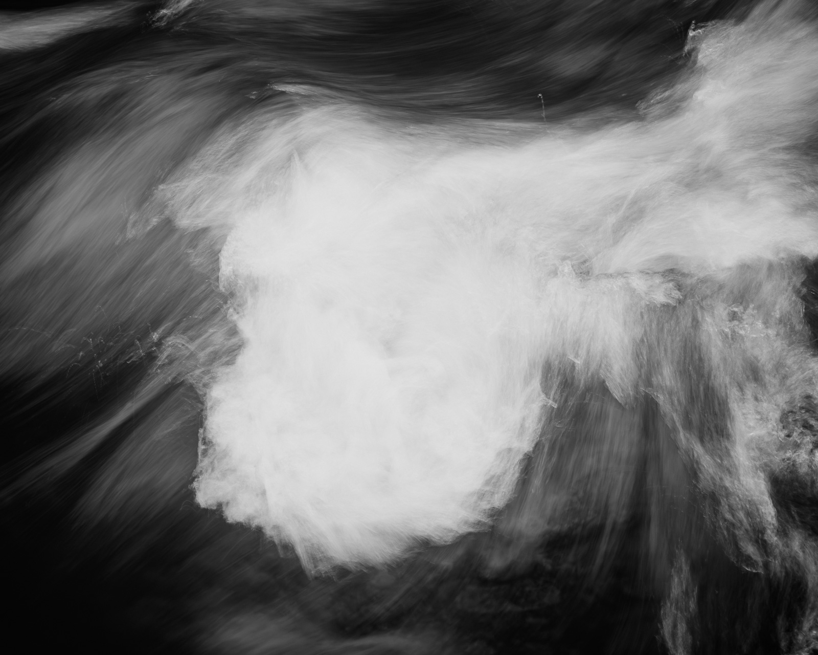 A dense mass of white water presses forward, momentarily holding its shape as darker currents sweep around it.