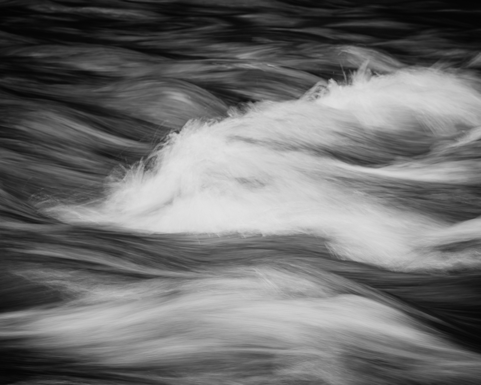 A bright swell of water rises briefly from the darker flow, forming a soft crest before being drawn back into the moving current.
