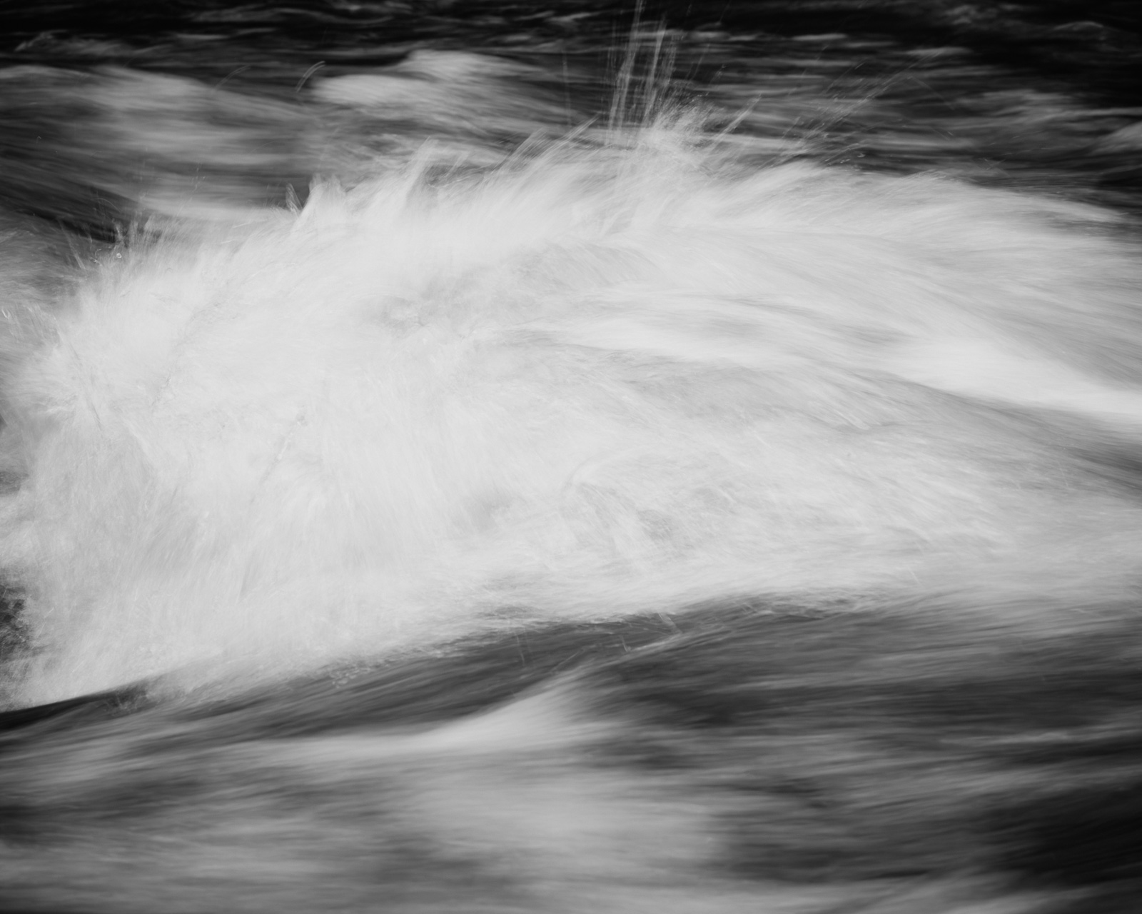A wide sweep of white water stretches across the frame, smoothing into darker layers as the current moves through.