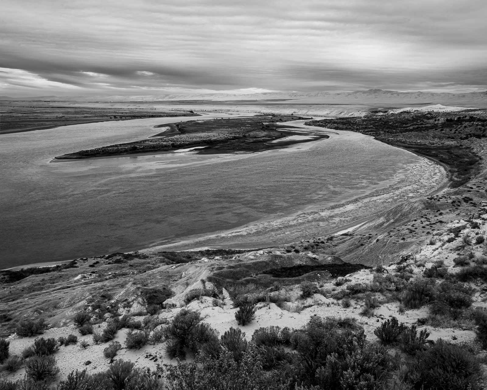 The Columbia River bends through the Hanford Reach, its wide channel bordered by sand, brush, and the pale forms of the White Bluffs.